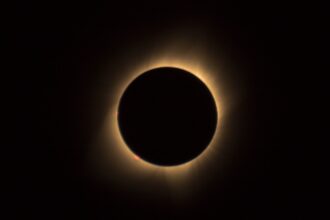 Photograph of a rare hybrid solar eclipse, showcasing the moon partially covering the sun, casting a shadow on Earth, with a radiant corona visible around the moon's silhouette.